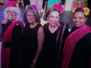 four brown women dressed in black with paper flowers in their hair.