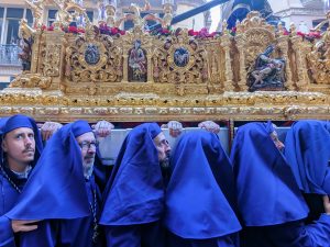 Men in blue robes and hoods carrying a throne with Jesus on top during Holy Week in Malaga, Spain