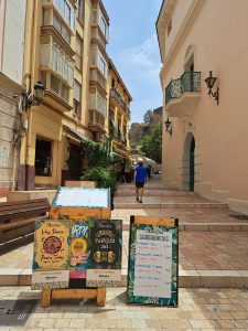 Shady street in Malaga with cafe signs in the foreground