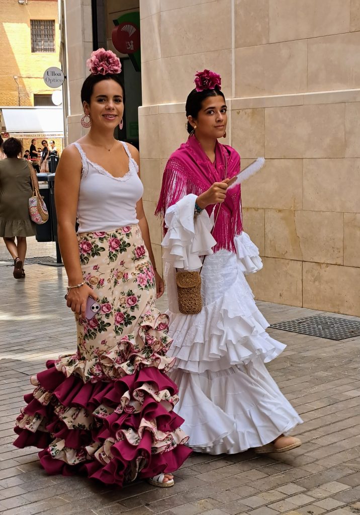 Two young women in Flamenco wear walking down a street in Malaga