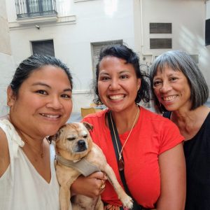 Three brown women, one of them holding a lapdog