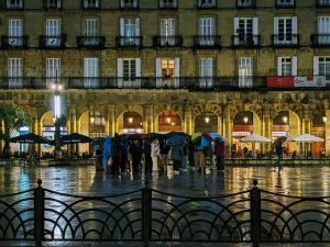 A group huddled under umbrellas in the middle of a plaza at night