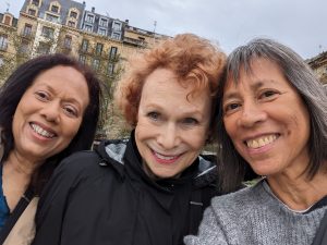 Three women, a redhead surrounded by two dark-haired women, on a windy day in Northern Spain