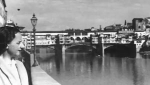 Black and white photo of a woman looking at a river in a European city