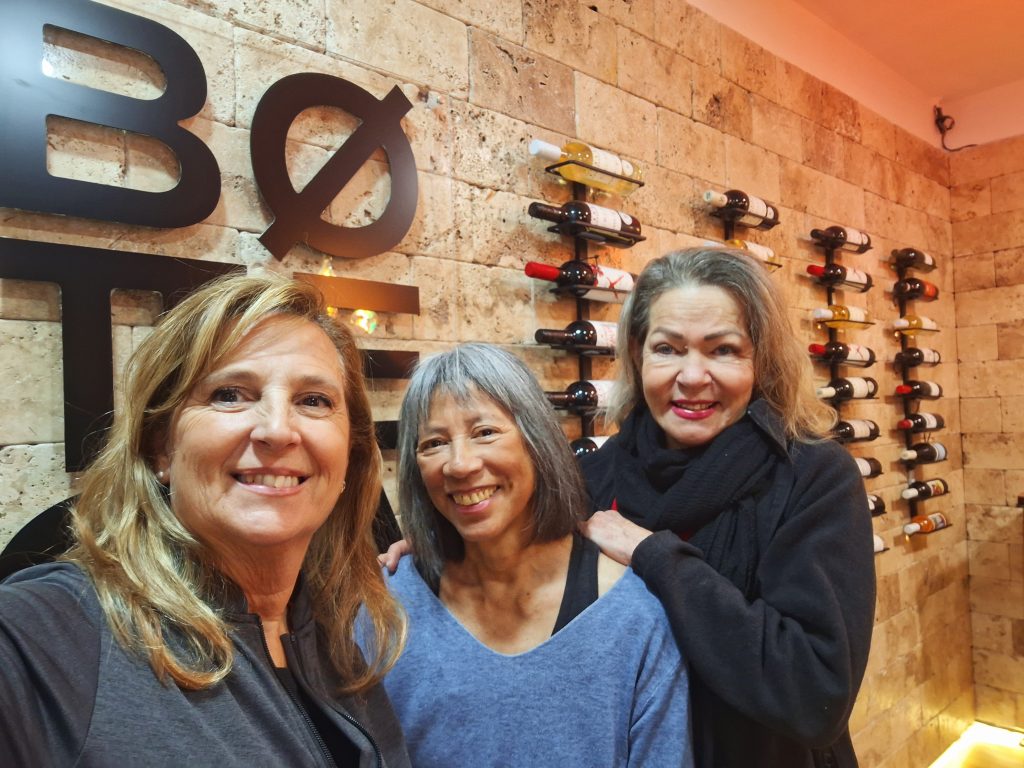Three women in front of a display of wines on the wall