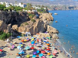 Beach with multicolored umbrellas with cliff and town in the background