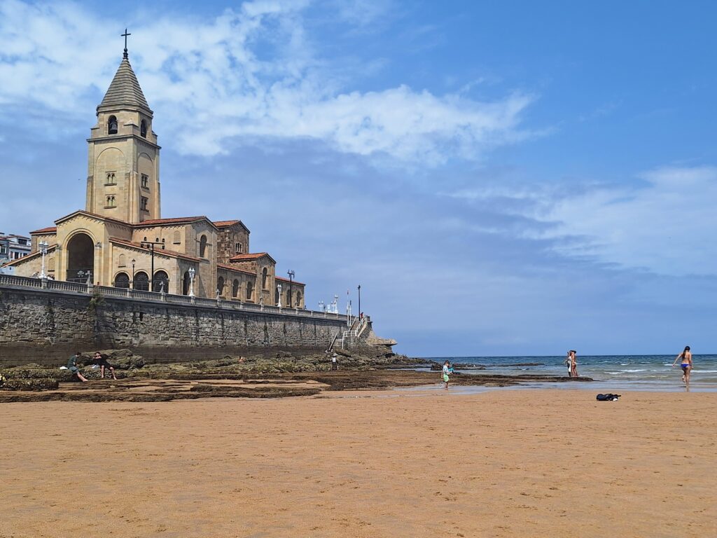 Expanse of San Lorenzo Beach with historic building in background in Gijon, Spain