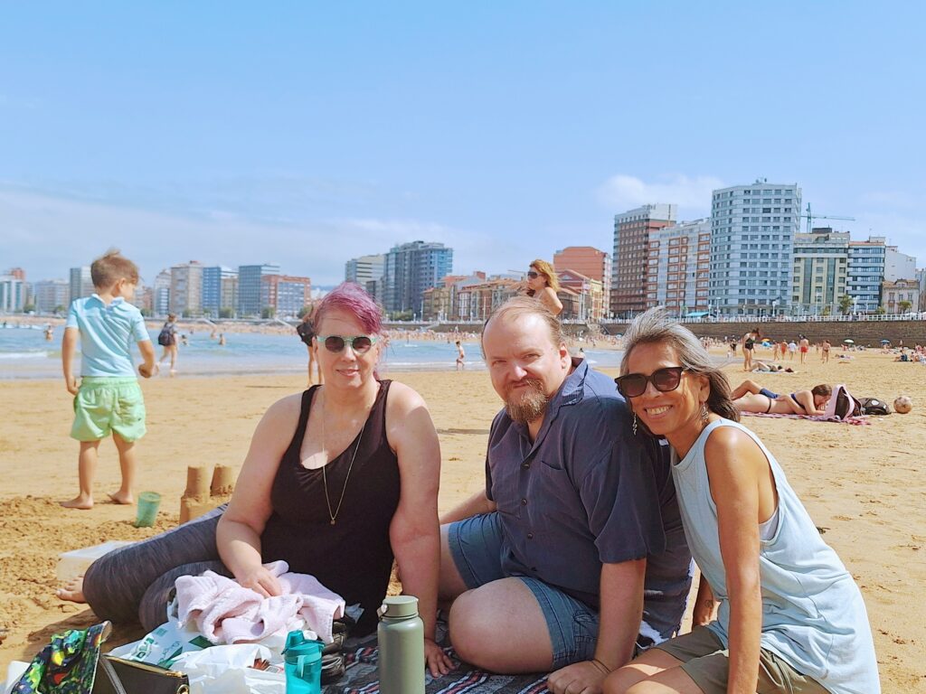 Three people sitting on the San Lorenzo Beach in Gijon, Spain