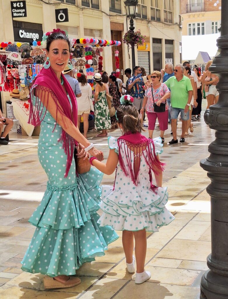 A woman in a green Flamenco dress facing the camera and her young daughter in a white Flamenco dress facing away from the camera