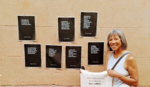 Woman standing against a wall with seven white-lettering-on-black-background signs.