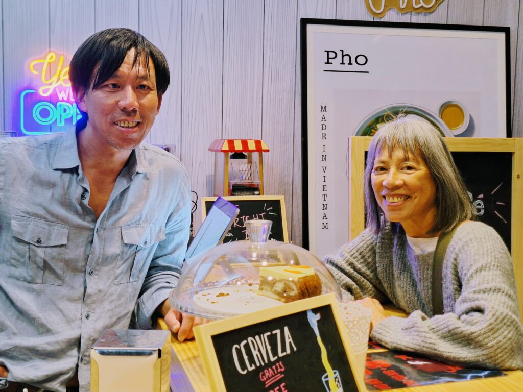 Vietnamese American man behind the counter of a cafe with a brown-skinned woman beside him on the other side of the bar