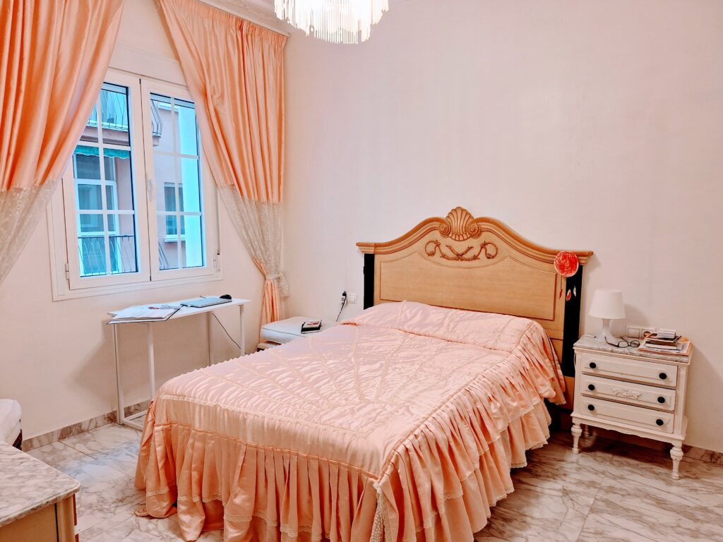 Bedroom with a pink ruffled bedspread and matching curtains, and a bedside table in French decor.