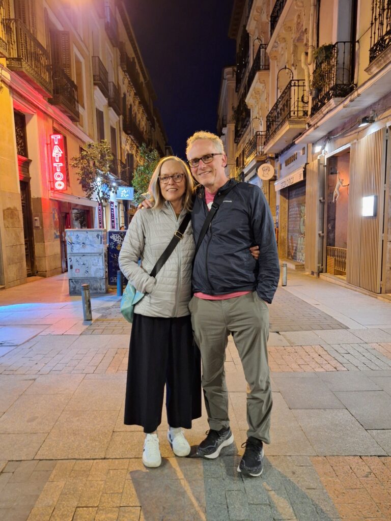 A man and a woman in a small Madrid street posing with arms around each other.