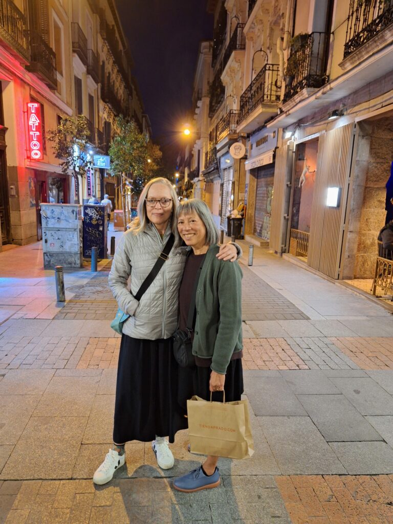 Two women in a narrow Madrid street at night, posing with arms around each other.