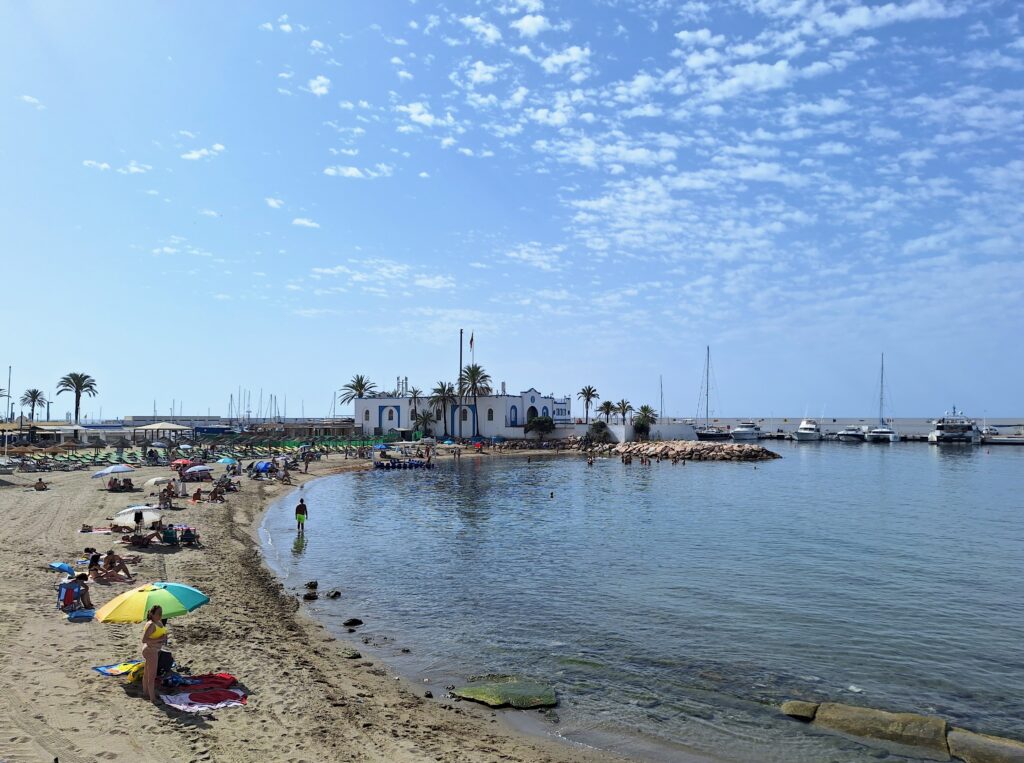 Beach with sunbathers and a typical Spanish style building in the background