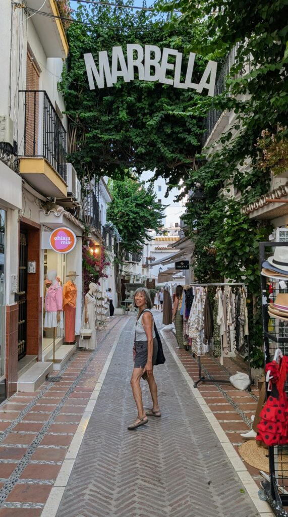 Woman turning to face camera on a cobblestone street with sign above that says Marbella