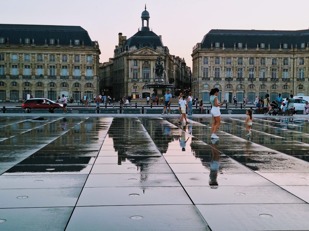 Neoclassical buildings mirrored in the wet stone plaza across the street in Bayonne, France