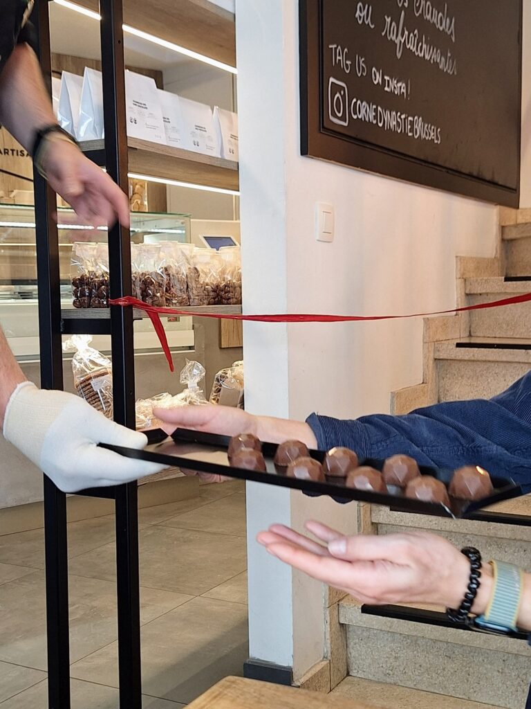A tray of chocolate candy being passed from one set of hands to another inside a candy shop
