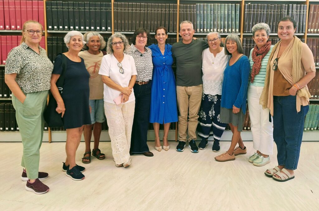 Ten women and a man pose in front of a shelf of books in a library