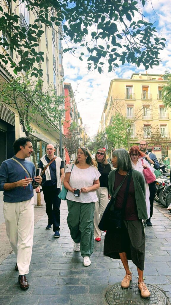 A group of people walk down a street in Madrid attentive to the tour guide