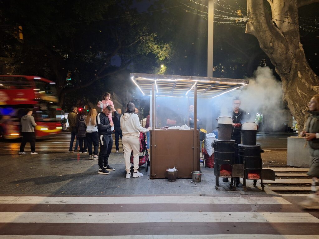 Night scene of a street vendor selling roasted chestnuts. Smoke rises from the barrels of roasting chestnuts.