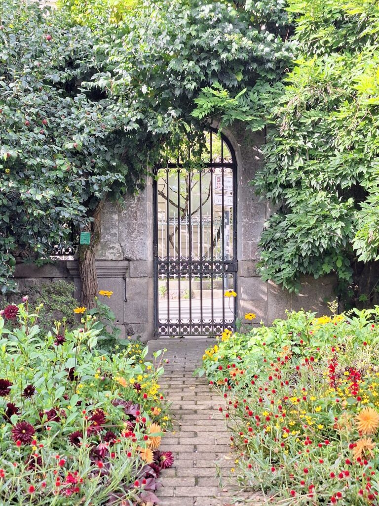 Arched gate with shrubbery surrounding it and beds of flowers in front of it in the botanical garden in Nantes, France