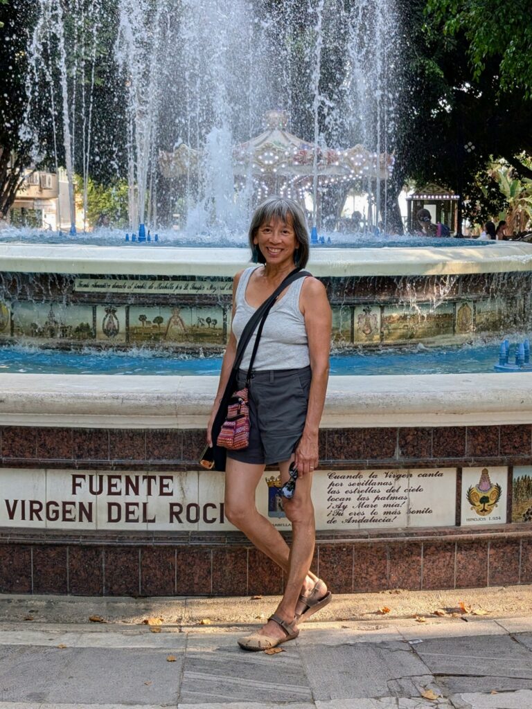 Woman in tank top and shorts standing in front of a fountain in Marbella, Spain.