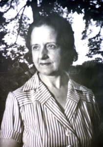 Black and white three-quarter portrait of Maria Zambrano when she was in her 50s. She's outdoors with trees behind her. Shre's wearing a striped dress.