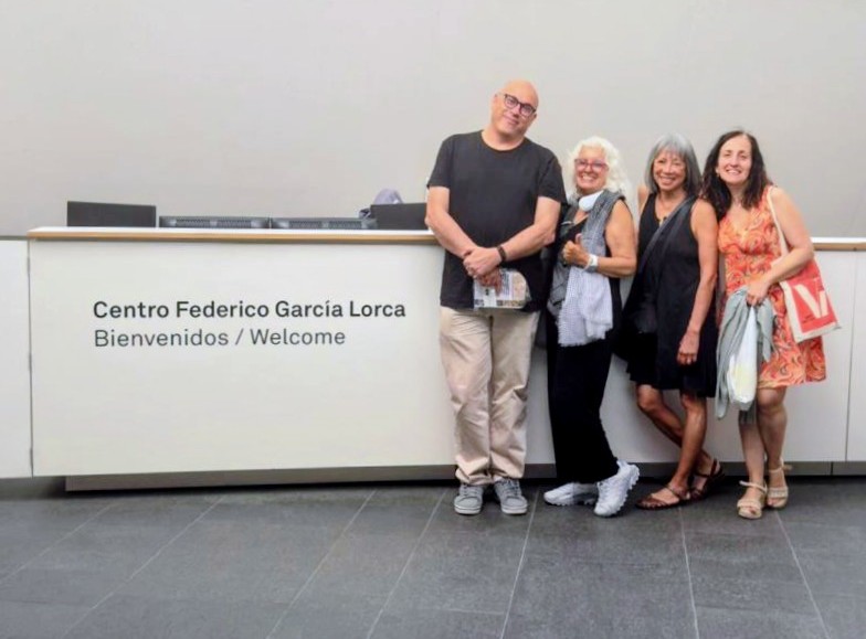 Four people stand in front of a long counter that reads Centro Federico Garcia Lorca Bienvenido/Welcome. The people are a tall, bald man with glasses and three women approximately the same height about a foot shorter than the man. They are facing the camera and smiling.
