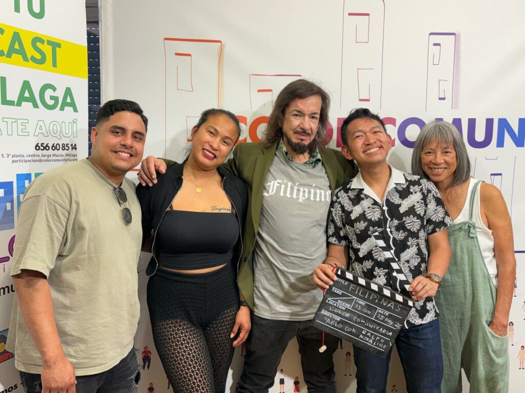 Five people stand together with arms around each others shoulders. In the middle is a long-haired bearded Spaniard. to his left is a thirtyish Filipino woman dressed sexily in black. Next to her is a thirtyish Venezuelan man with a friendly face. To the right of the Spaniard in the middle is a thirtyish Filipino man with glasses and a black and white print shirt. Next to him is a woman with a pageboy cut dressed in a white tank top and green linen overalls.
