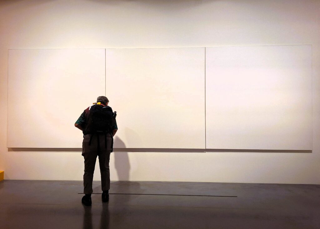 A woman examines a painting of three panels painted white.