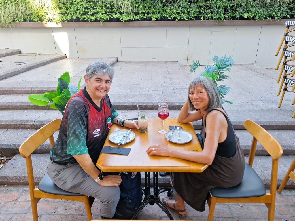 Two women areseatd at a cafe table outdoors with drinks on the table and empty plates.