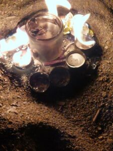 Small lit tea candles circle a larger lit candle on a picnic plate in the sand.