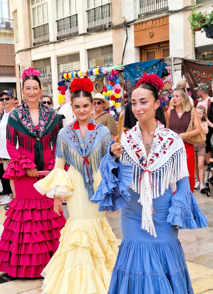 Three young women dressed in colorful flamenco outfits pose for the camera