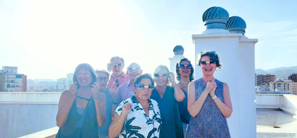 A group og eight people on a rooftop wearing special dark glasses for viewing the eclipse